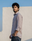 Man wearing a light-colored shirt and dark jeans against a clear blue sky.
