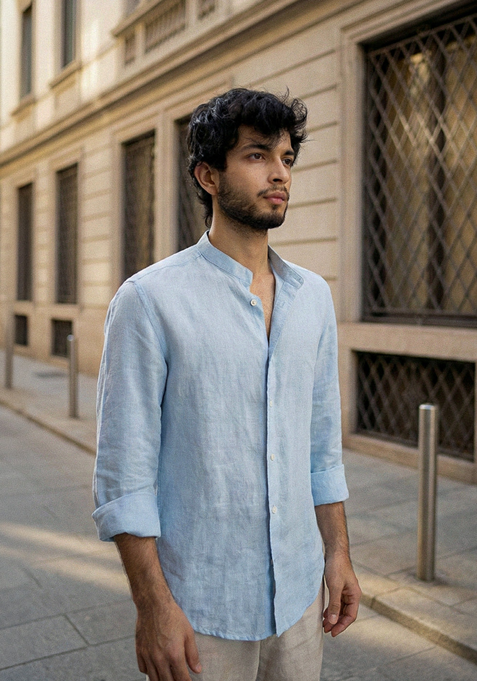 Man wearing a light blue shirt standing on a street with a building in the background