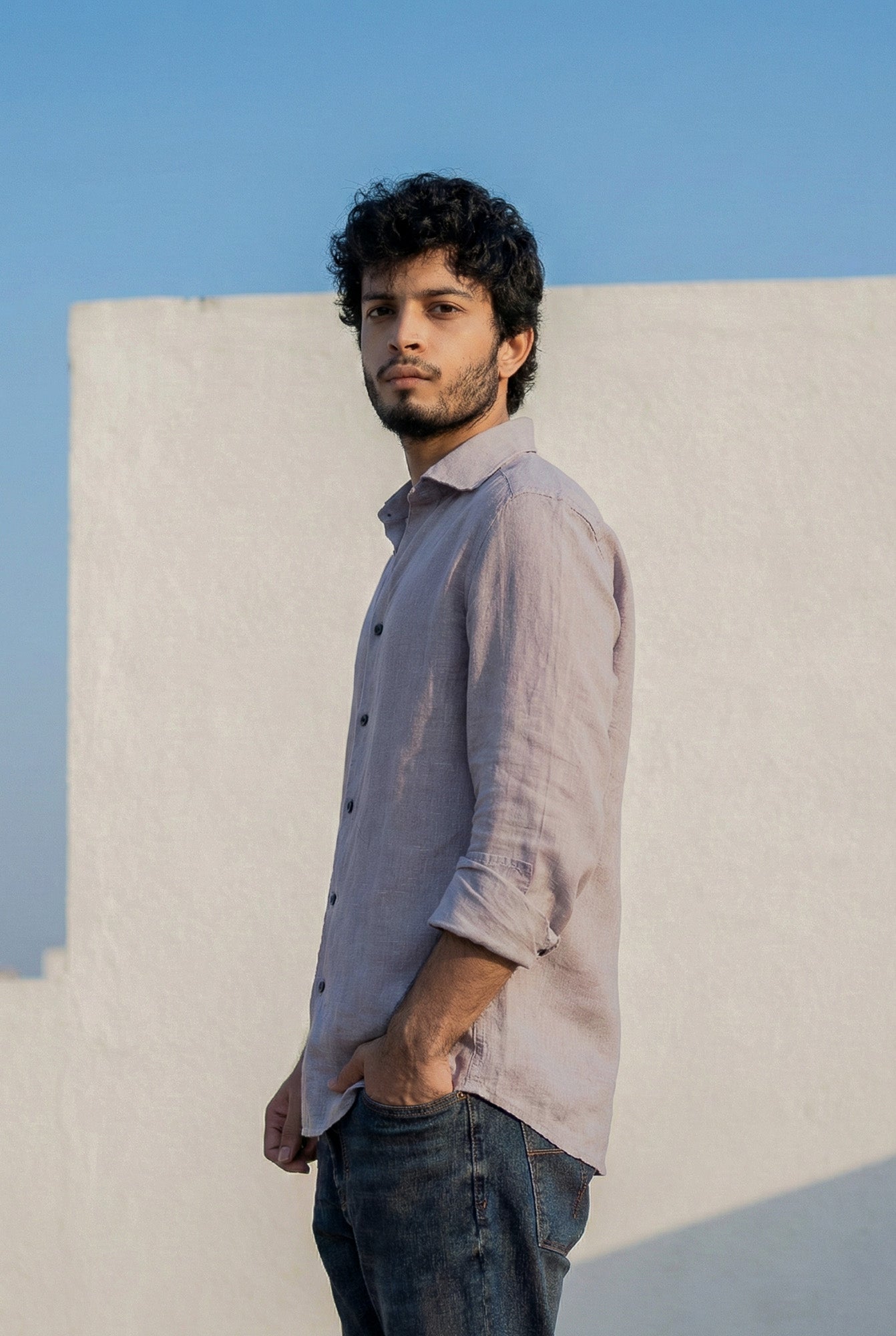 Man wearing a light-colored shirt and dark jeans against a clear blue sky.
