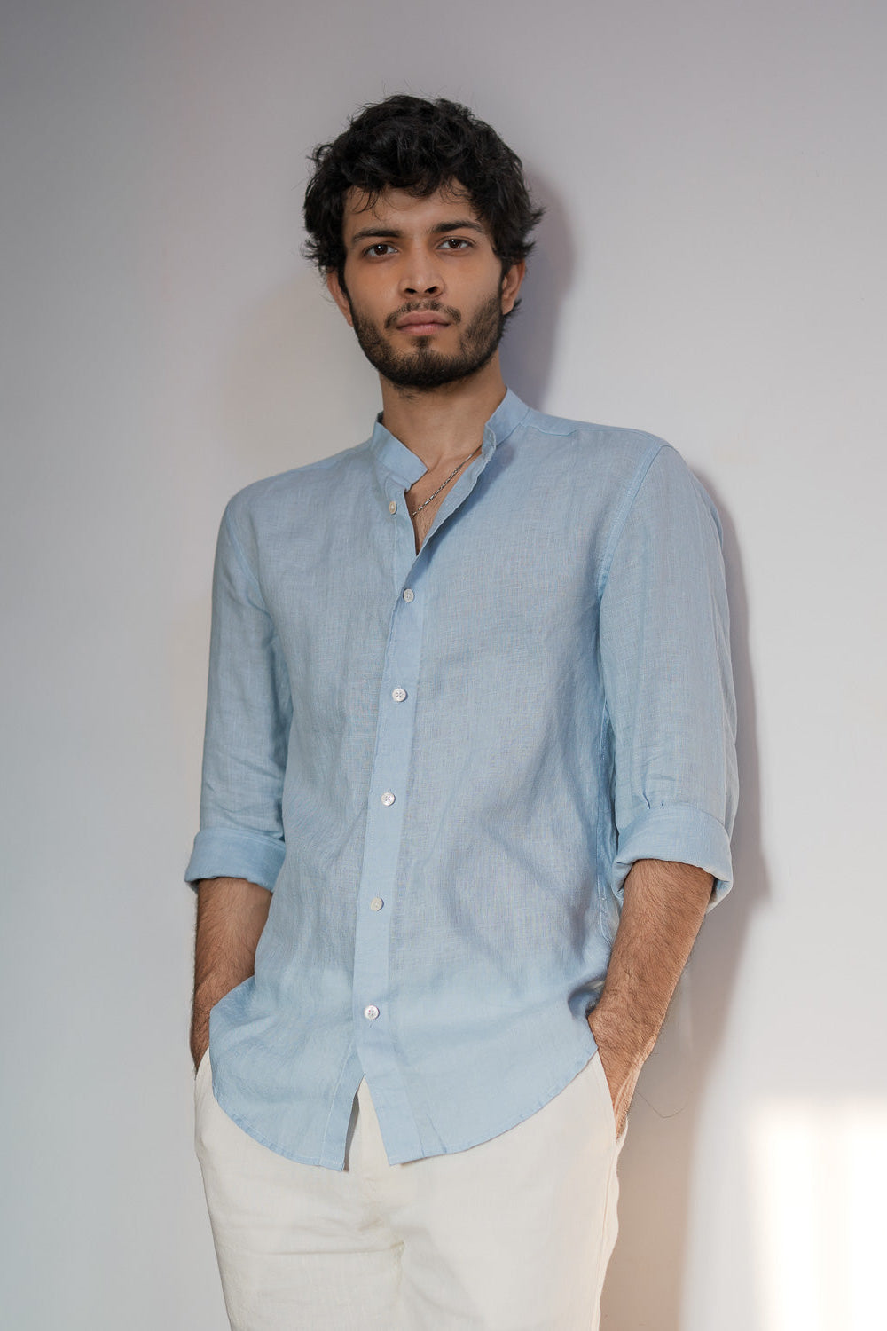 Man wearing a light blue shirt and white pants against a plain background